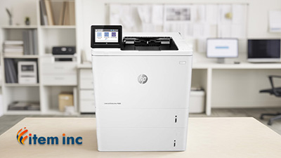 HP LaserJet Enterprise M609 printer on a desk in a modern office setting, with the Item Inc. logo in the corner.