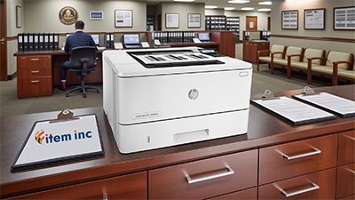 HP LaserJet Pro M402n printer on a wooden counter in a government office setting, with blank clipboards in the foreground and a clerk working at a desk in the background.