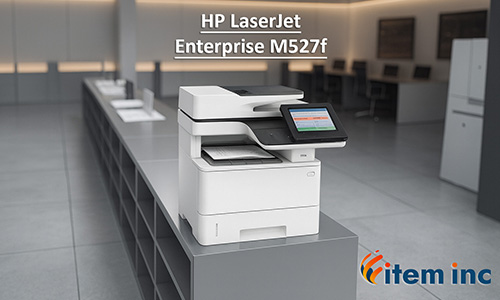 HP LaserJet Enterprise M527f multifunction printer on a sleek gray cabinet in a modern office, with blurred desks and chairs in the background, and 'item inc' logo at the bottom right.