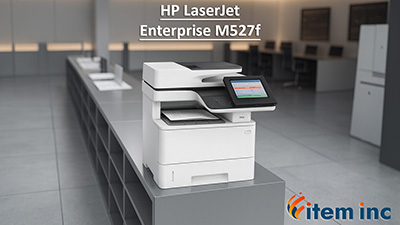 HP LaserJet Enterprise M527f multifunction printer on a sleek gray cabinet in a modern office, with blurred desks and chairs in the background, and 'item inc' logo at the bottom right.