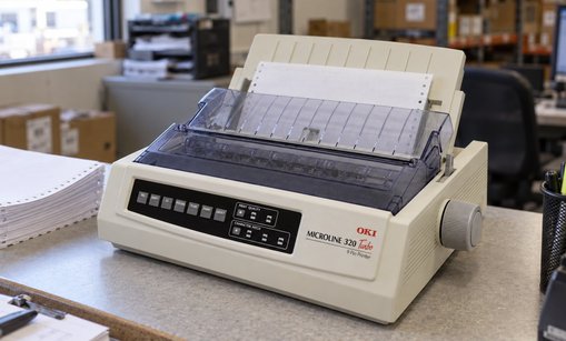 OKI Microline 320 Turbo dot matrix printer loaded with continuous forms on a warehouse office counter